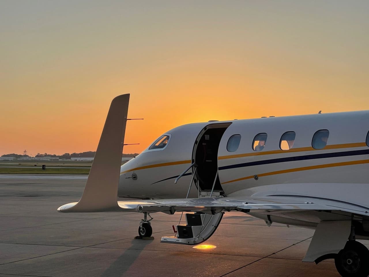 A business jet on the ramp at sunset, its airstair door open under an orange sky
